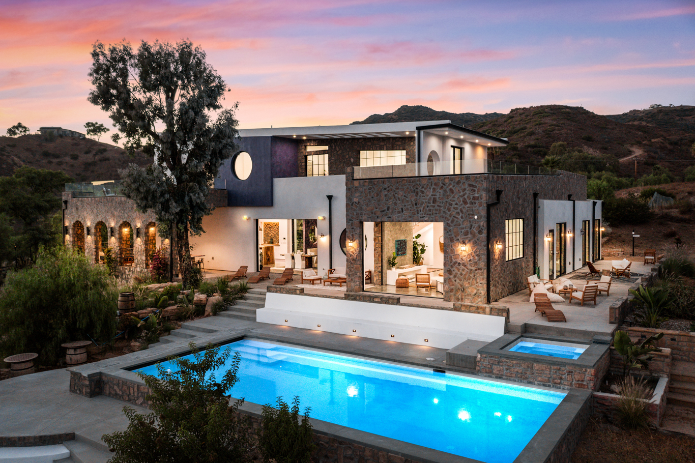 Maliview, a stone and plaster Malibu hillside home with a lit pool at dusk
