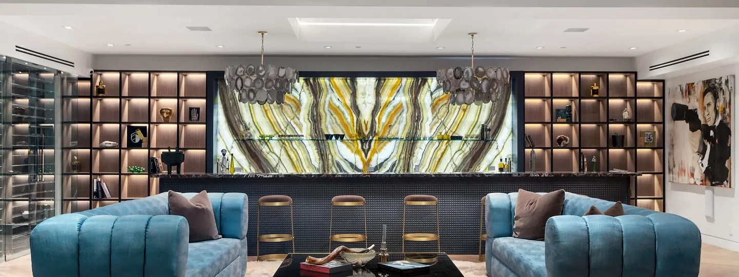 Blue tufted sofas and a brass-based table facing a backlit stone bar wall, an interior by Apel Design