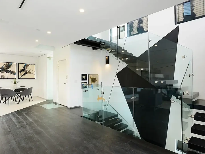 Glass balustrades and black angled panels frame an open stair beside a dining area, an interior by Apel Design