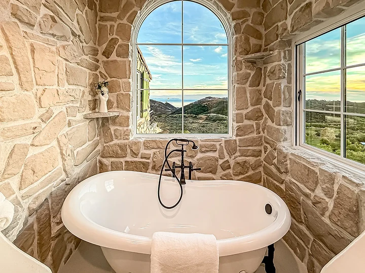 Clawfoot tub beneath an arched window in a stone alcove, at Mintcello in Malibu, by Apel Design
