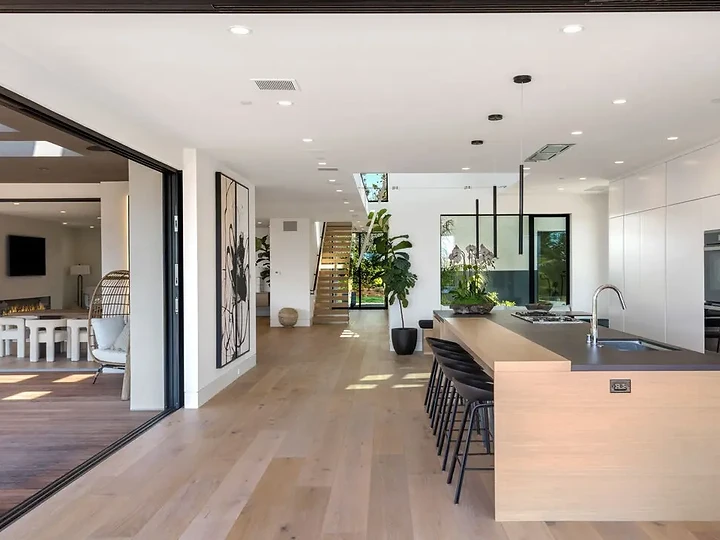 Long kitchen island in pale wood beside a glass wall opened to the garden, an interior by Apel Design