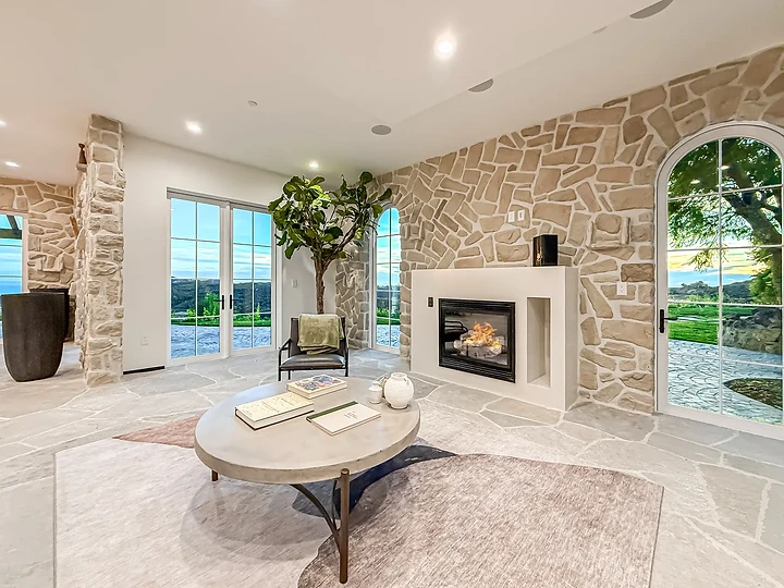 A stone-walled sitting room with a fireplace and an arched garden door, at Mintcello in Malibu, by Apel Design