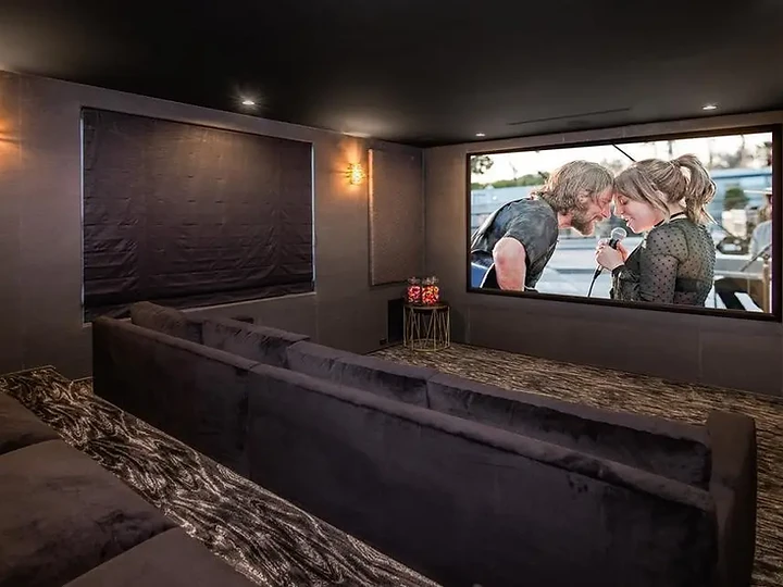 A dark-walled theater with plush sofas in two tiers and warm wall sconces, an interior by Apel Design