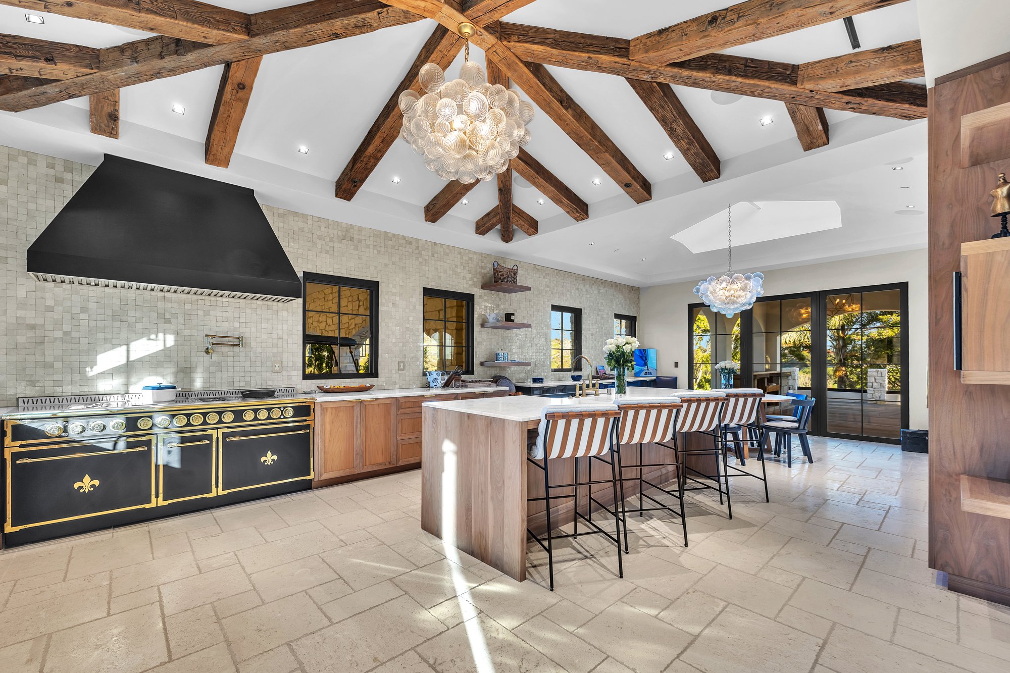 The kitchen under radiating timber beams, with the range and the island, Merritt Estate in Malibu by Apel Design
