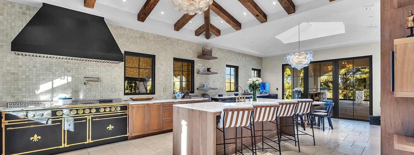 Kitchen under radiating timber beams with a black range and a long island, at Merritt Estate in Malibu, by Apel Design