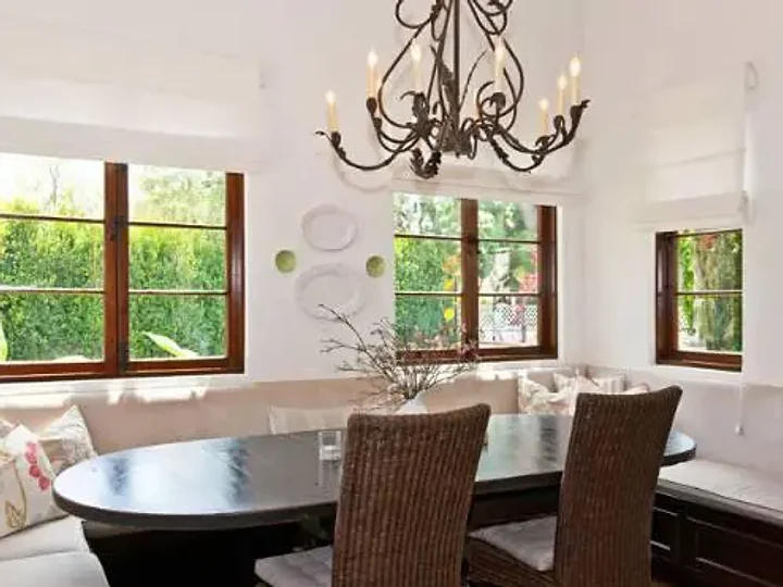 An upholstered banquette wraps an oval table beneath an iron chandelier and garden windows, an interior by Apel Design