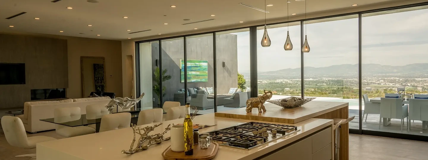 Kitchen island with a cooktop and glass pendants, open to a dining room and a city view, an interior by Apel Design