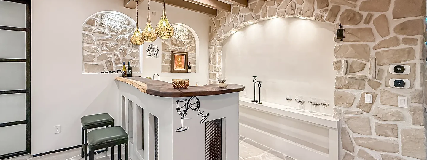 Three pendants over a curved timber bar beside a lit arched stone niche, at Mintcello in Malibu, by Apel Design