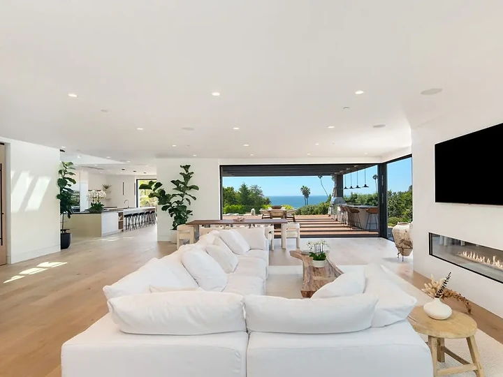A white sectional facing a linear fireplace, with the ocean view beyond, an interior by Apel Design