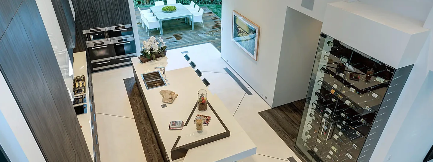 A long white island seen from above beside a glass wine case and a terrace, an interior by Apel Design