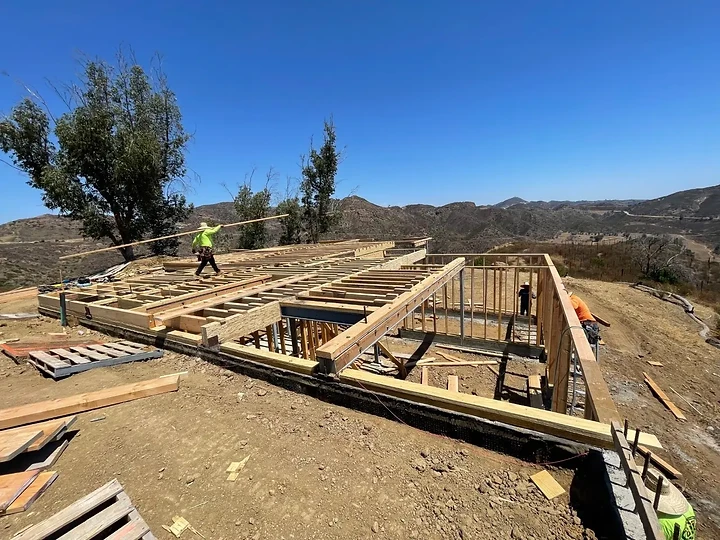 Floor framing and walls going up at Oya, with the hills beyond