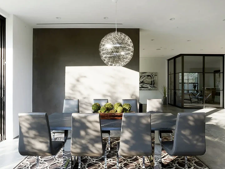 A wire sphere pendant over a dark dining table, with sunlight falling across the floor, an interior by Apel Design