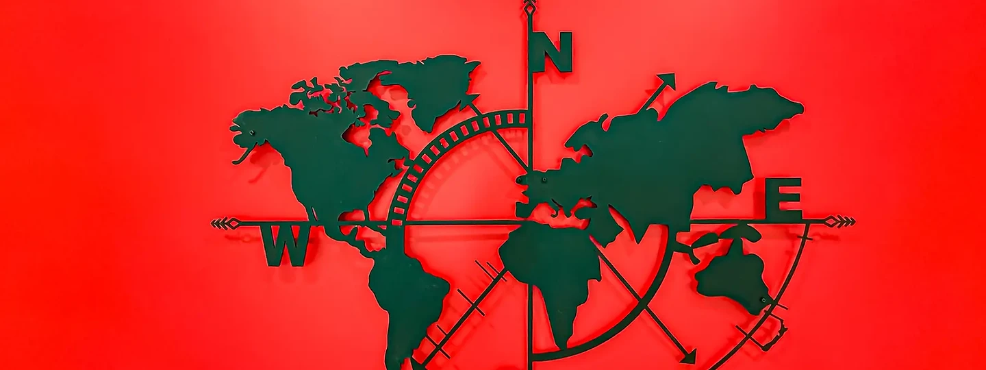 Dark green world map and compass sculpture on a red wall, at The Aviator in Malibu, by Apel Design