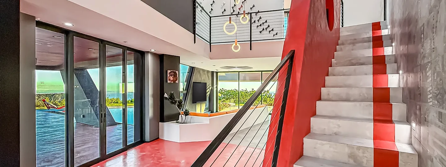A red and gray stair climbs a double-height room beside glass walls, at The Aviator in Malibu, by Apel Design