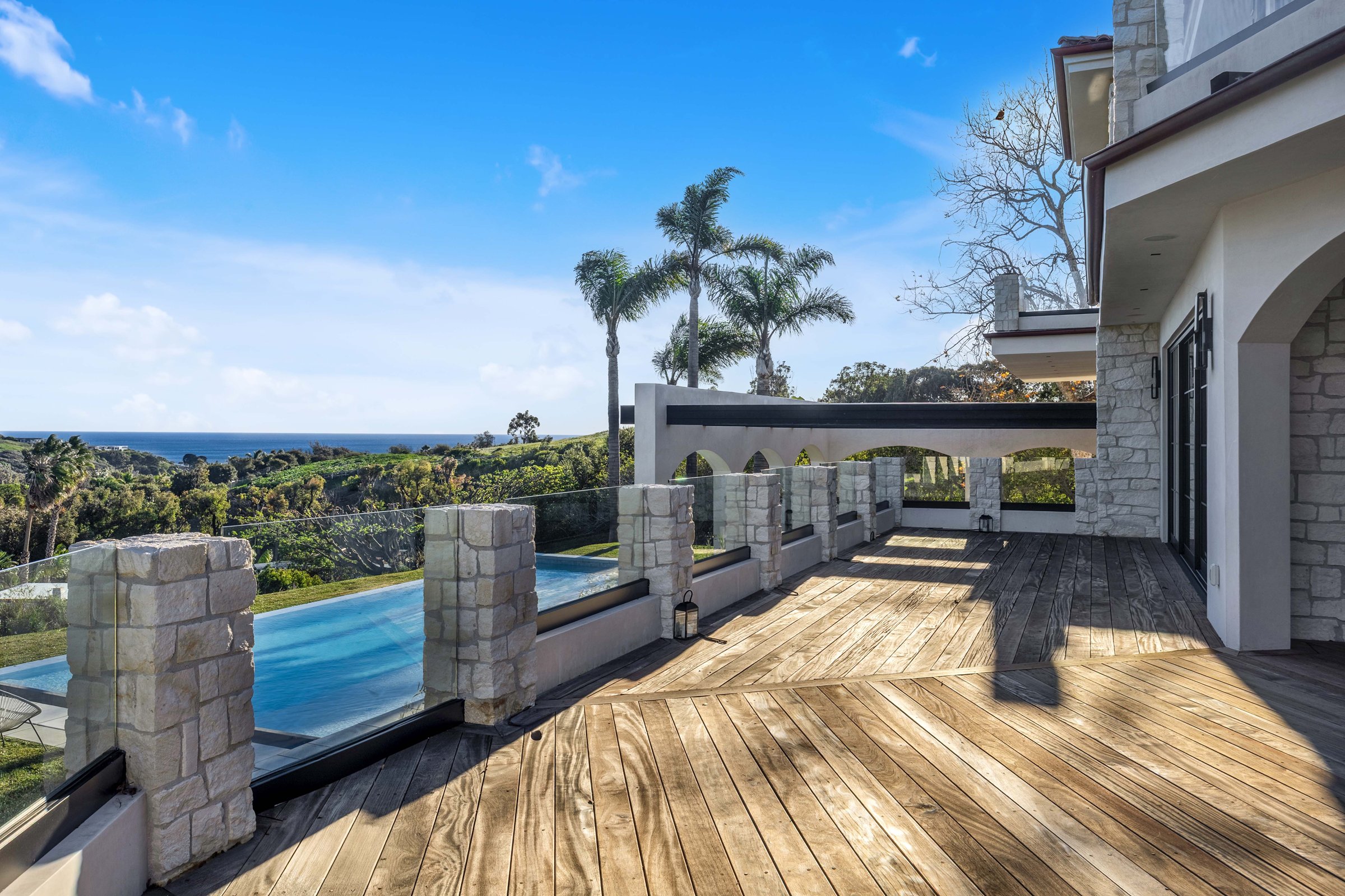 An upper terrace edged with stone piers and glass, above the pool, Merritt Estate in Malibu by Apel Design