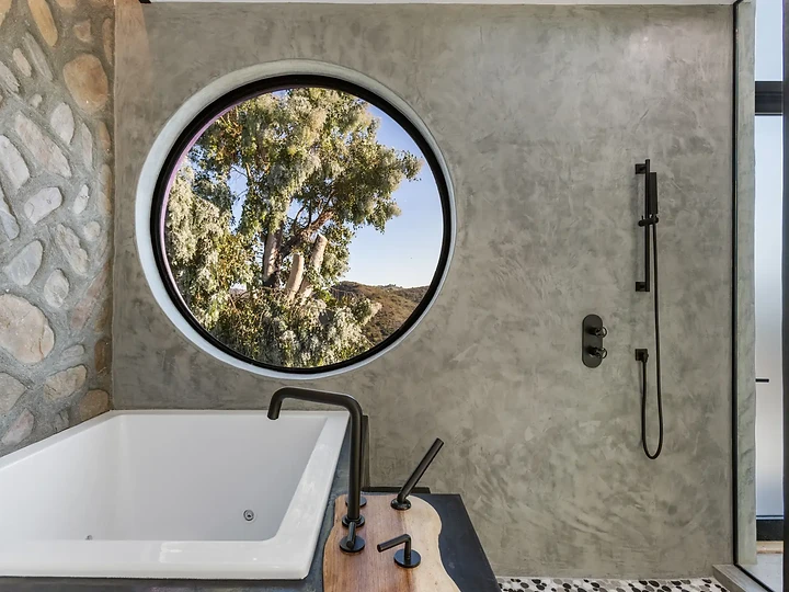 White tub and shower under a round window in a plaster bath, at Maliview in the Malibu Mountains, by Apel Design