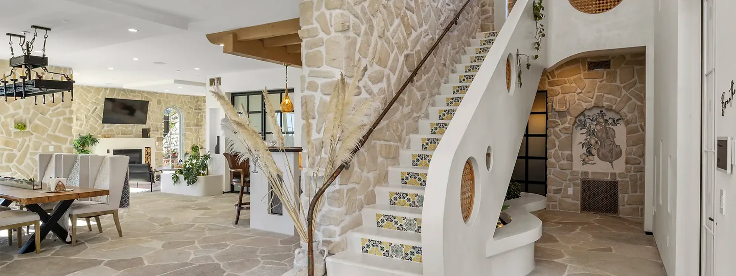 A curving white stair with patterned tile risers climbs beside a stone wall, at Mintcello in Malibu, by Apel Design