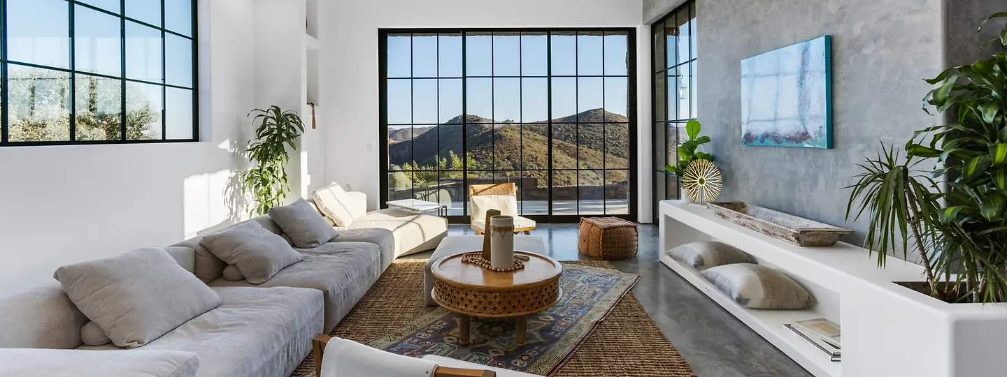 Steel windows frame the mountains beyond a long gray sofa, at Maliview in the Malibu Mountains, by Apel Design