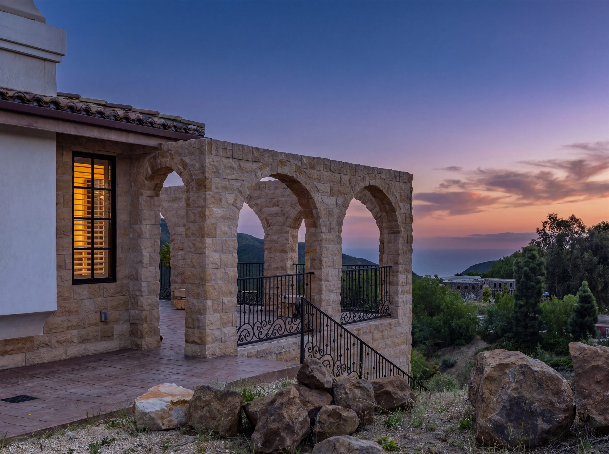 Stone loggia arches at Oya lit at twilight above the coastal hills