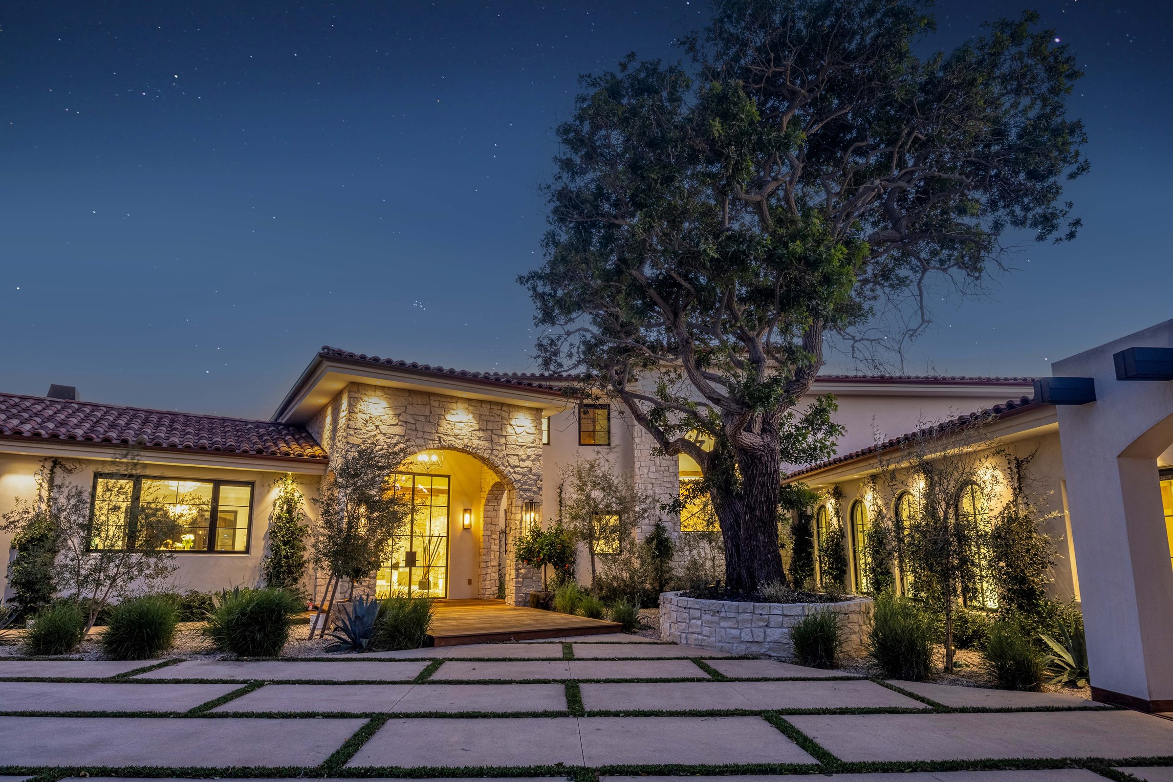 The entry court at night, around a mature tree in a stone planter, Merritt Estate in Malibu by Apel Design