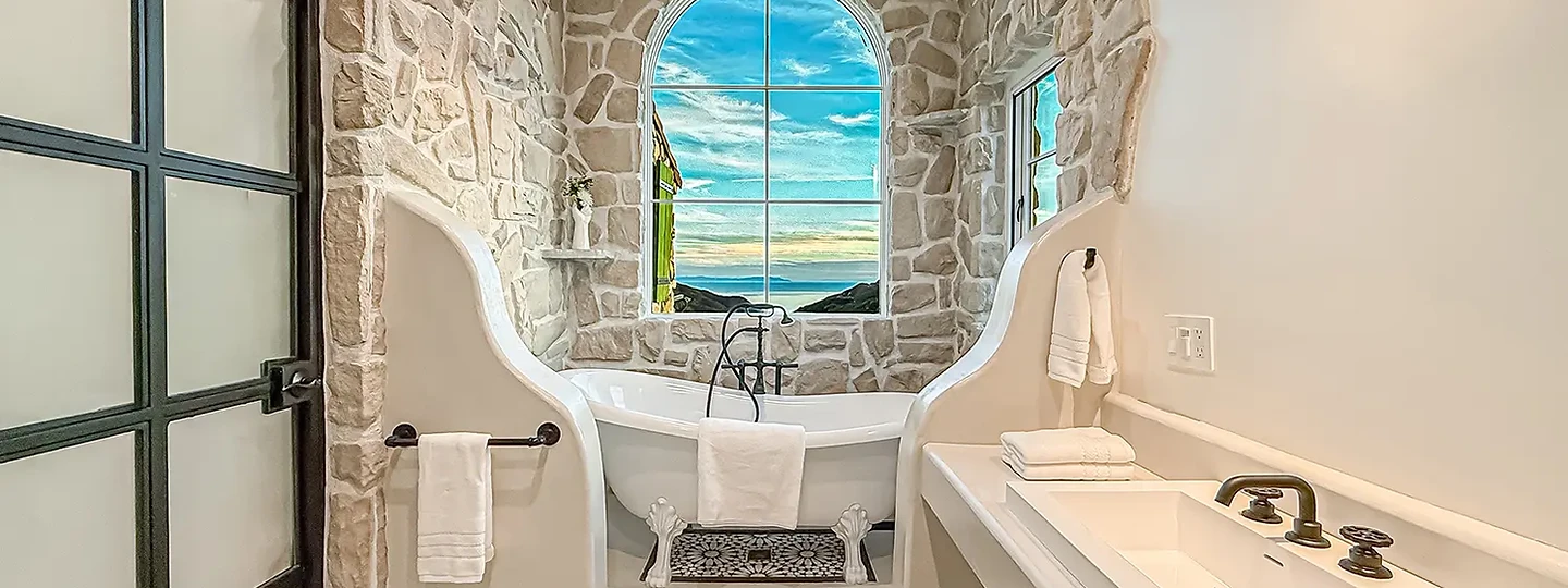 Soaking tub in a sculpted stone alcove beneath an arched window, at Mintcello in Malibu, by Apel Design
