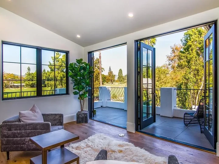 A sitting room with tall black-framed French doors open to a balcony and treetops, an interior by Apel Design