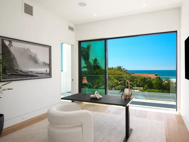A black desk and a curved white chair before sliding glass and an ocean view, an interior by Apel Design