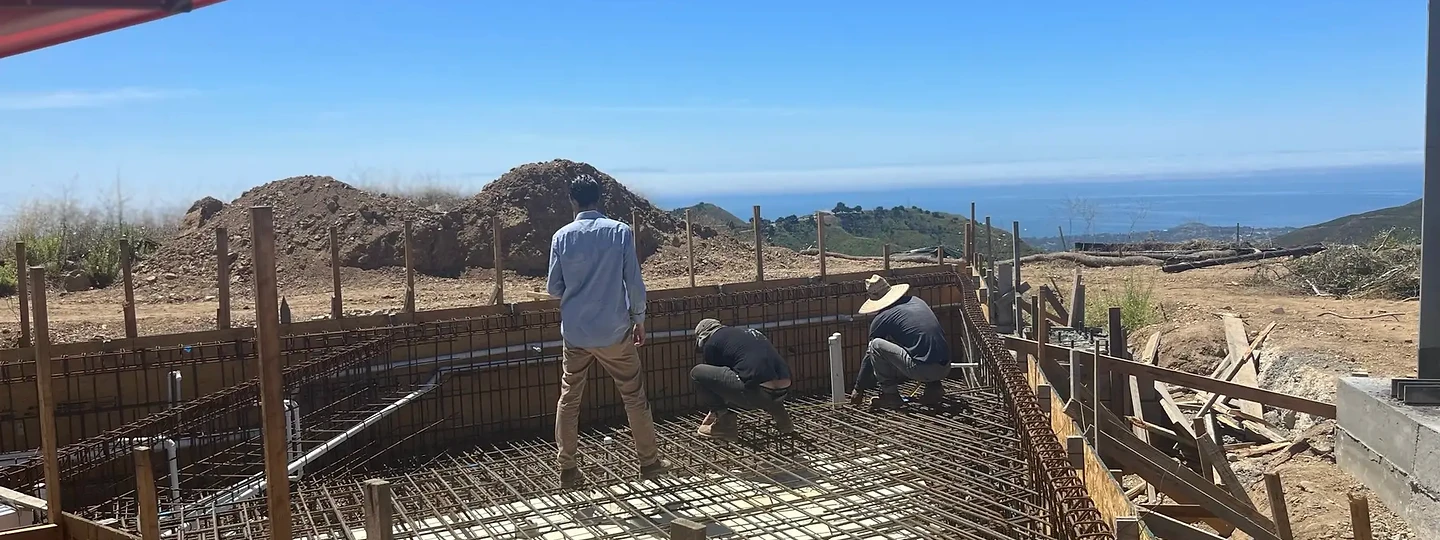 Crew tying rebar for a pool shell above the coastline
