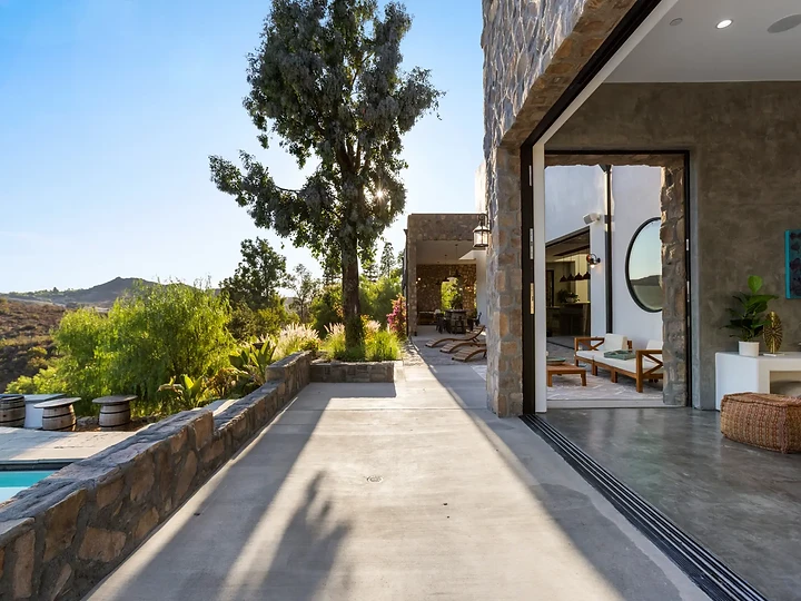 A stone-walled walk passing a wide opening into a lounge, at Maliview in the Malibu Mountains, by Apel Design