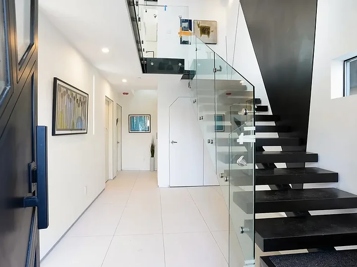 Black treads beside a glass rail and a black wall plane in a white hall, an interior by Apel Design