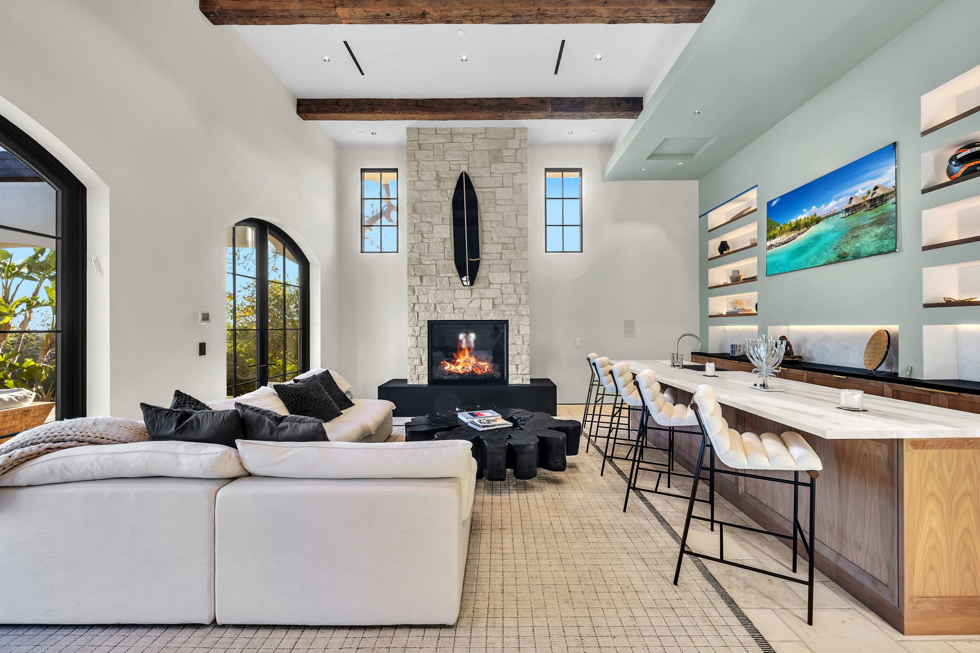 The great room, centred on a stone fireplace wall with a bar alongside, Merritt Estate in Malibu by Apel Design