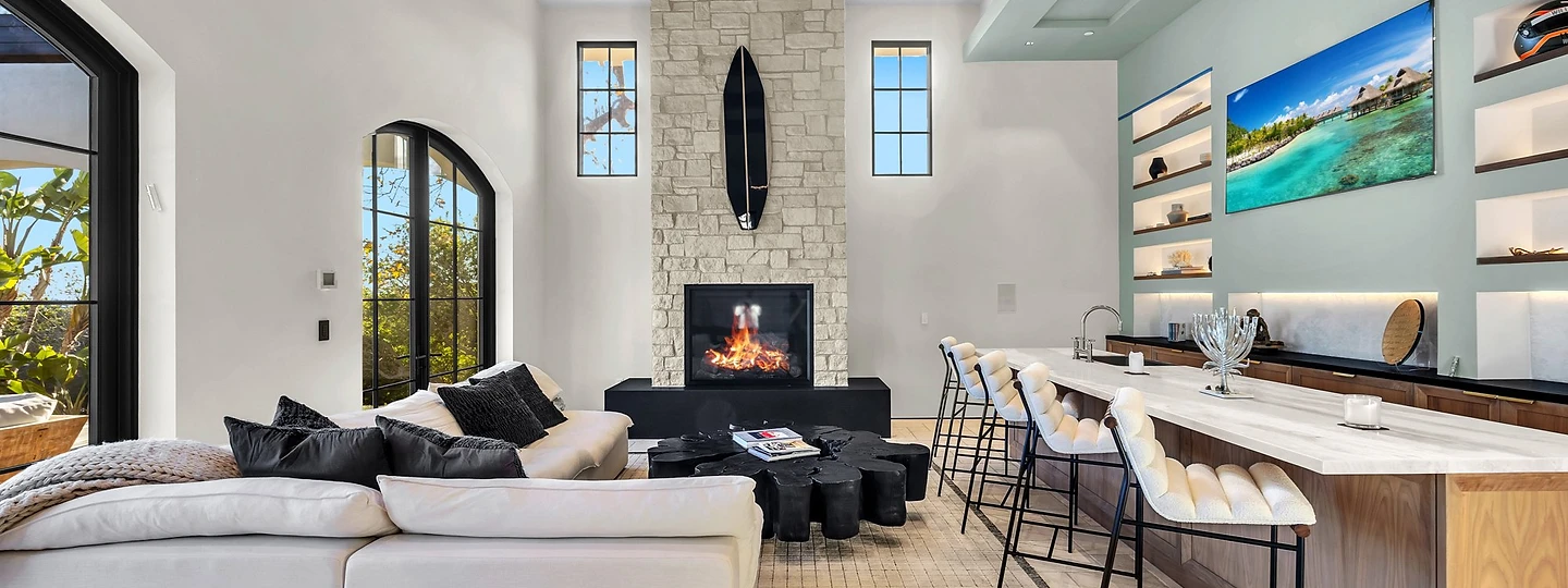 The great room's tall stone fireplace wall, with a bar alongside, at Merritt Estate in Malibu, by Apel Design