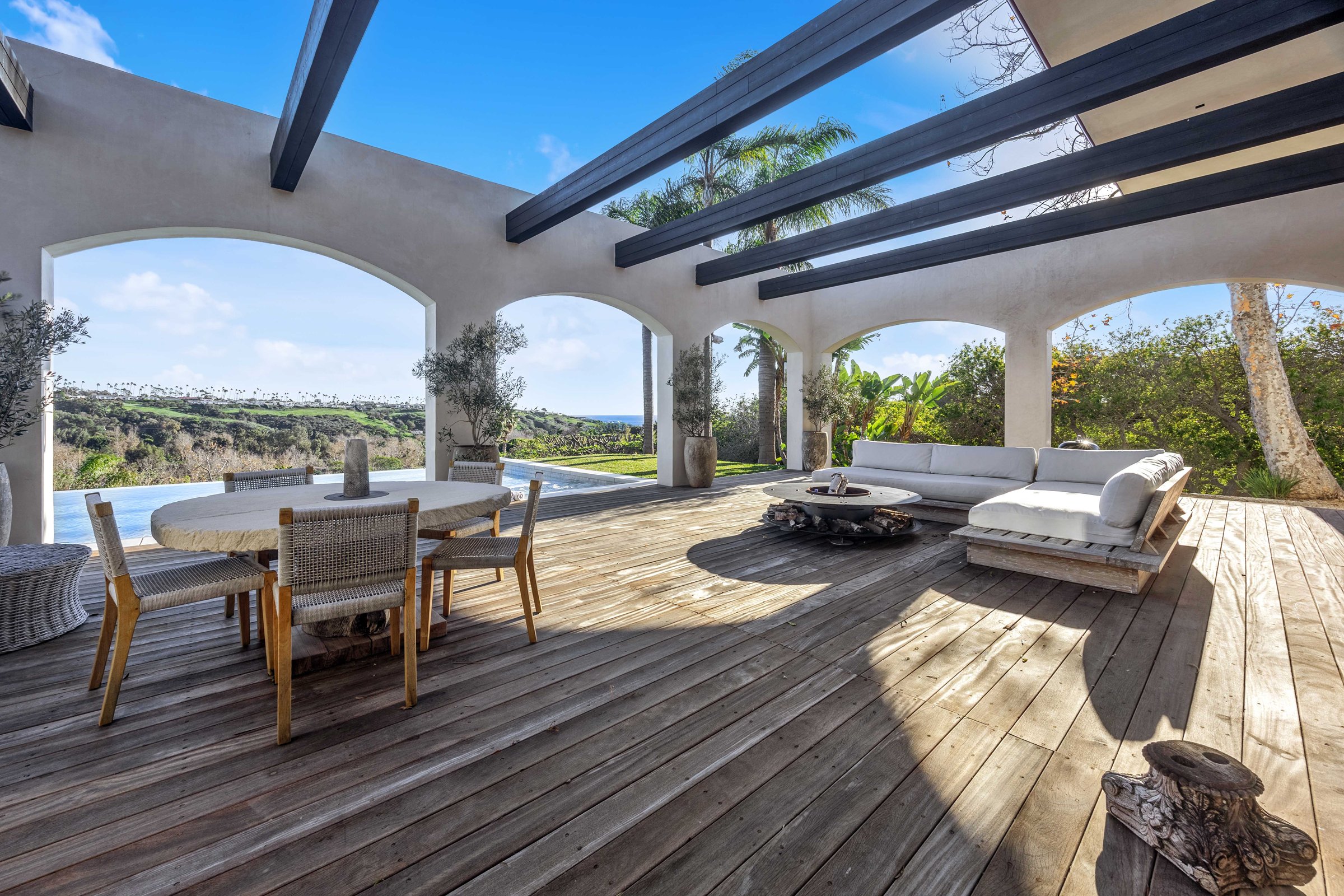 The covered loggia, with open dark beams over a timber deck, Merritt Estate in Malibu by Apel Design