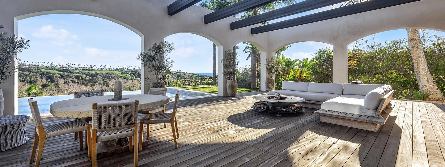A covered loggia with open dark beams over a timber deck, at Merritt Estate in Malibu, by Apel Design