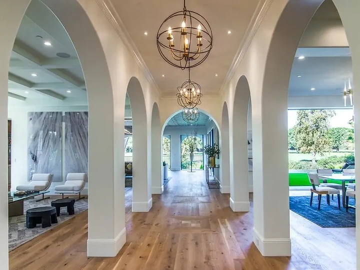 A hall of white arches under orb chandeliers, opening to living and dining rooms, an interior by Apel Design