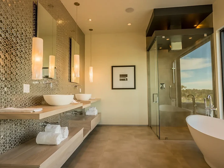 Bath with twin basins on floating wood shelves, a mosaic wall, glass pendants and a freestanding tub, an interior by Apel Design
