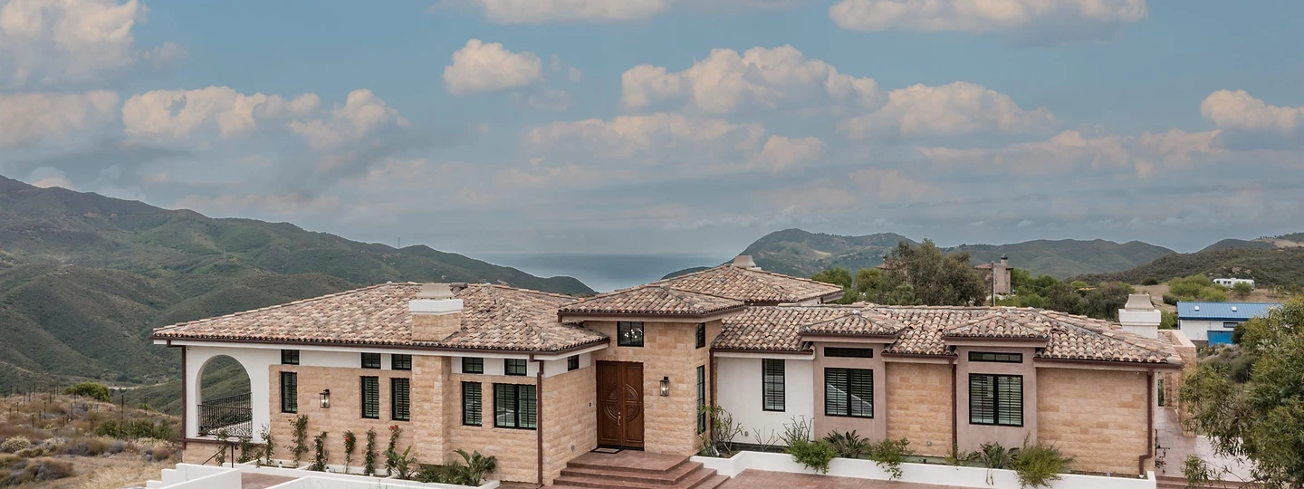 The completed hillside residence at Oya, with tile roof, stone arches and a terraced entry court above the hills