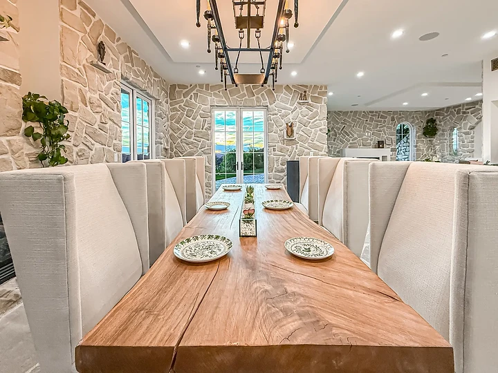 High-backed upholstered chairs line a thick plank table beneath an iron chandelier, at Mintcello in Malibu, by Apel Design