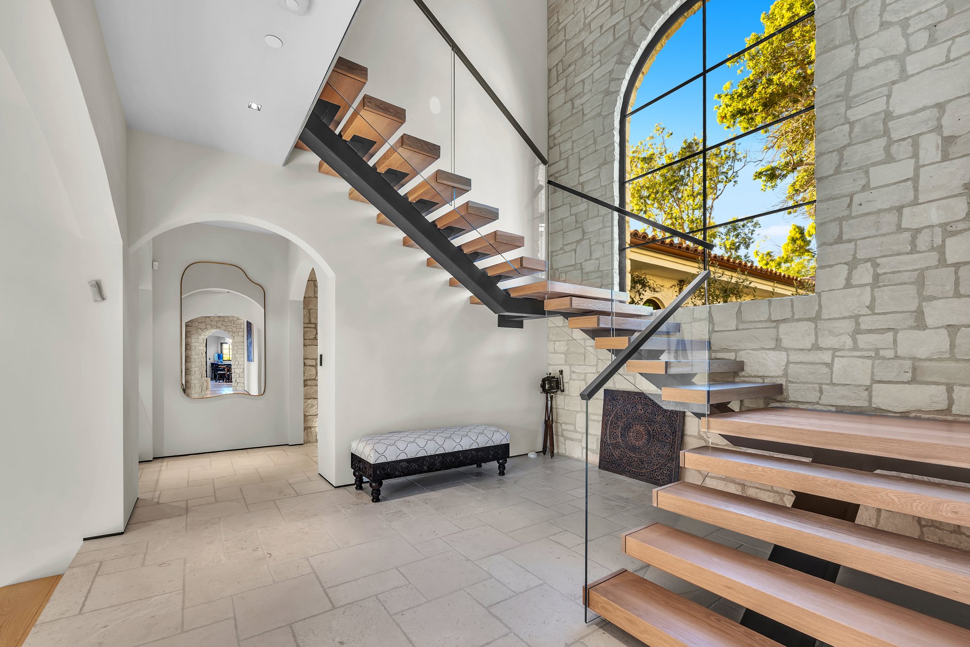 An open-riser timber stair beside a stone wall and an arched window, Merritt Estate in Malibu by Apel Design