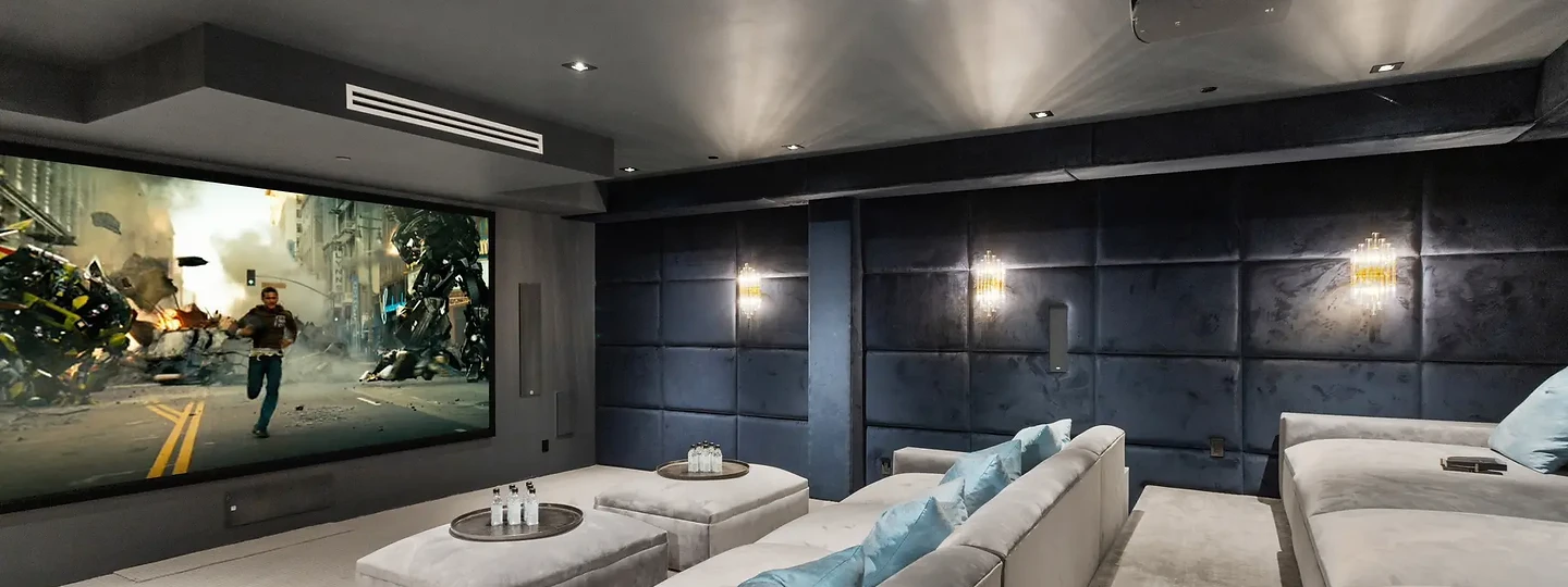 A home theater with upholstered wall panels and tiered pale sofas facing a large screen, an interior by Apel Design