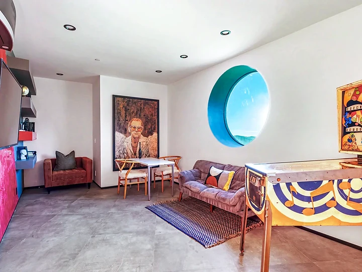 A game room with a vintage pinball machine and a round window, at The Aviator in Malibu, by Apel Design