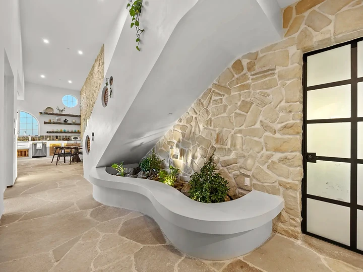 A sculpted white planter curves out from a stone wall beneath the stair, at Mintcello in Malibu, by Apel Design