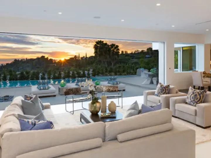 A living room with pale sofas, open along one side to a terrace at sunset, an interior by Apel Design