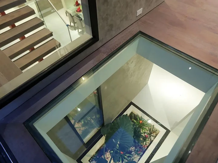 A glass floor panel looks down to a planted light well beside an open stair, an interior by Apel Design