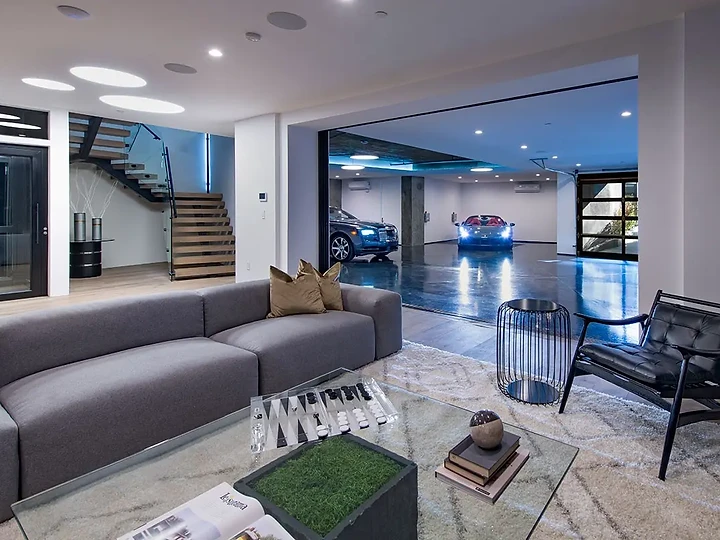 A grey lounge that opens to a lit gallery of cars beyond, an interior by Apel Design