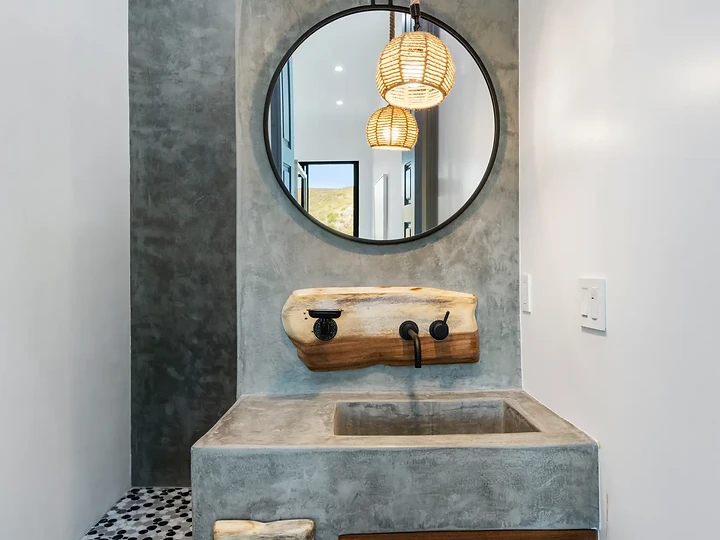 Concrete basin with a timber spout under a round mirror and woven pendants, at Maliview in the Malibu Mountains, by Apel Design