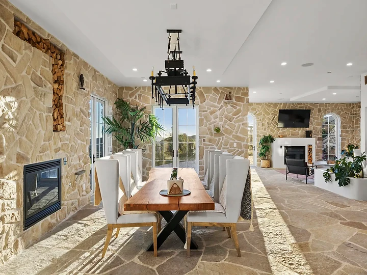 A timber dining table under an iron lantern, framed by stone walls, at Mintcello in Malibu, by Apel Design