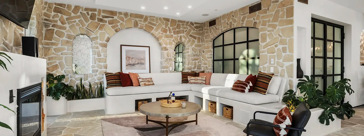 A curved white sofa set into a stone-walled living room beside a fireplace, at Mintcello in Malibu, by Apel Design