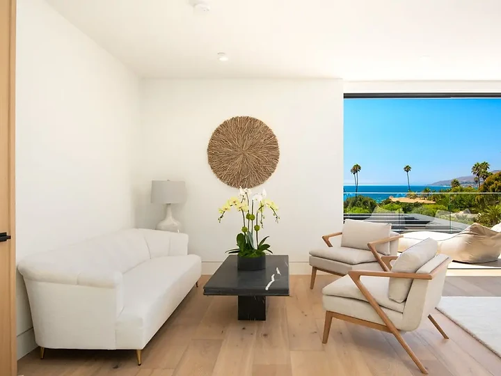 A white sofa, stone table with orchids and a woven wall disc facing the ocean, an interior by Apel Design