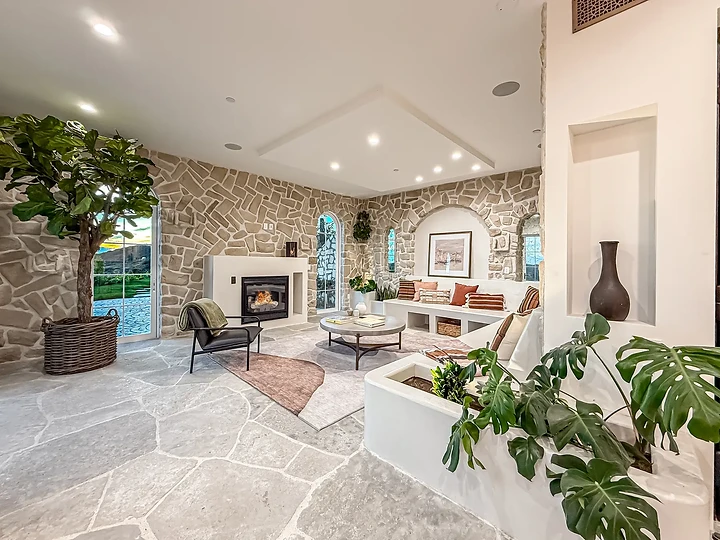 A stone-walled sitting room with a white fireplace, arched windows and potted trees, at Mintcello in Malibu, by Apel Design